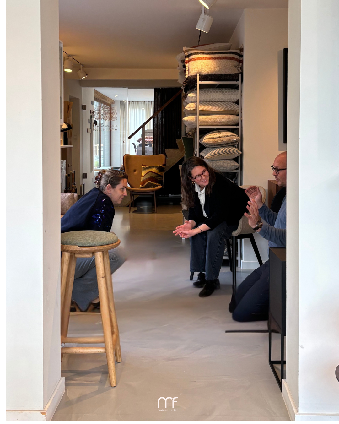 Drie personen in gesprek in een interieurwinkel, omringd  zitmeubels, terwijl ze samen een ontwerp- en materiaalkeuze bespreken.