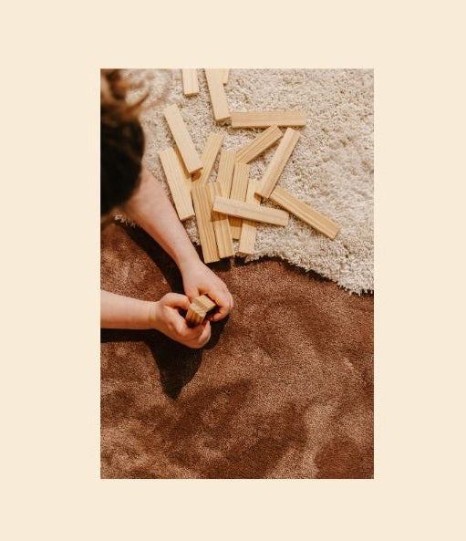 Spelend kind met houten blokjes op een Rhythm modulair tapijt. Earth low Moon high. Future-proof circulair design.