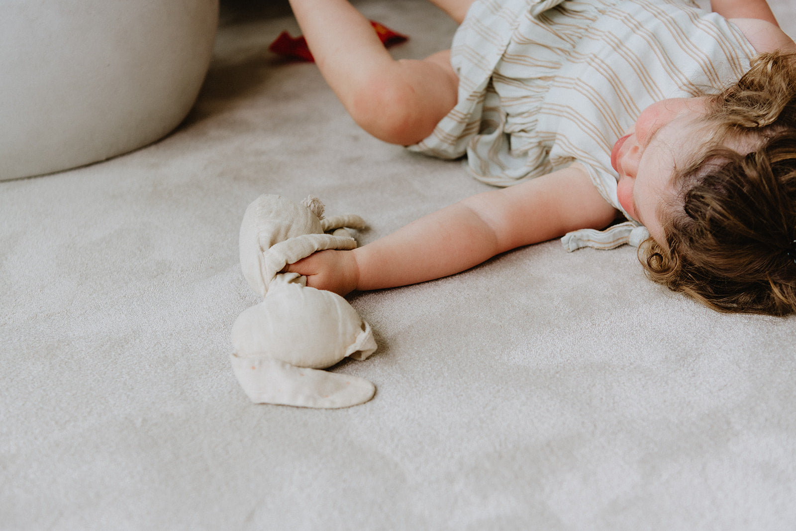 Sfeerbeeld interieur met kindje en knuffel op zacht beiegkleurig vloerkleed.