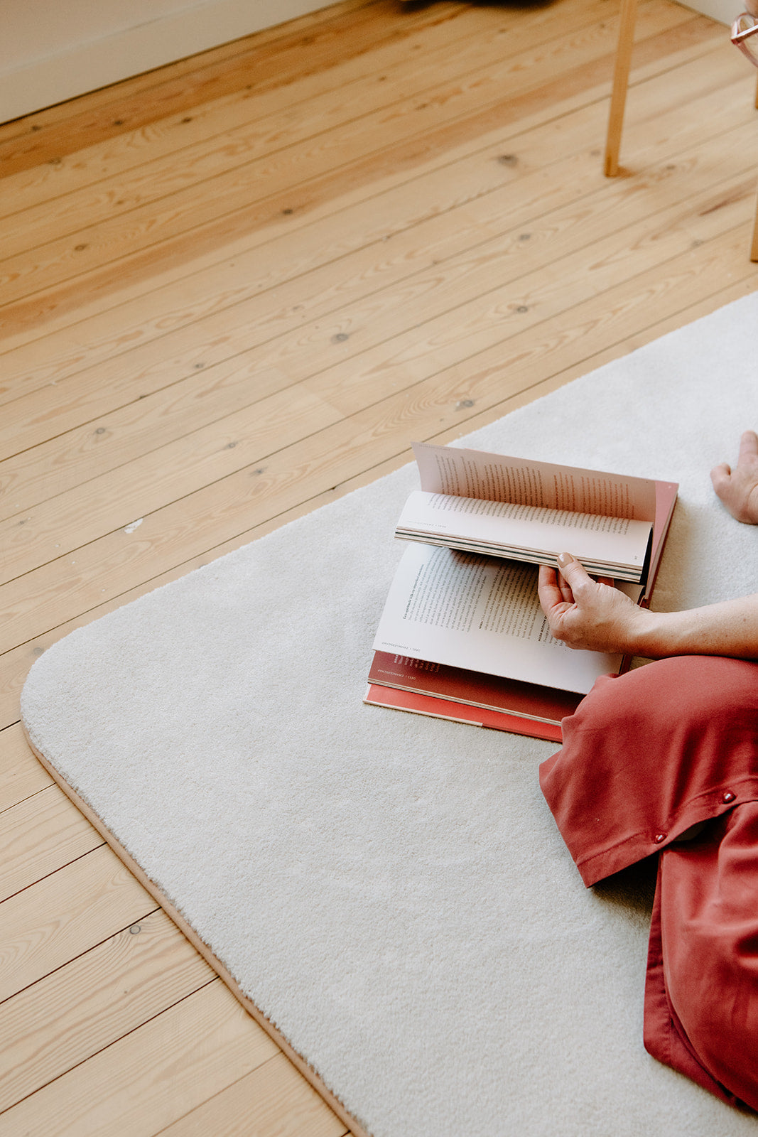 Zacht, ecologisch rechthoekig tapijt met ronde hoeken en blush kleurrand op houten vloer, onder een openliggend boek en deel van een vrouw.