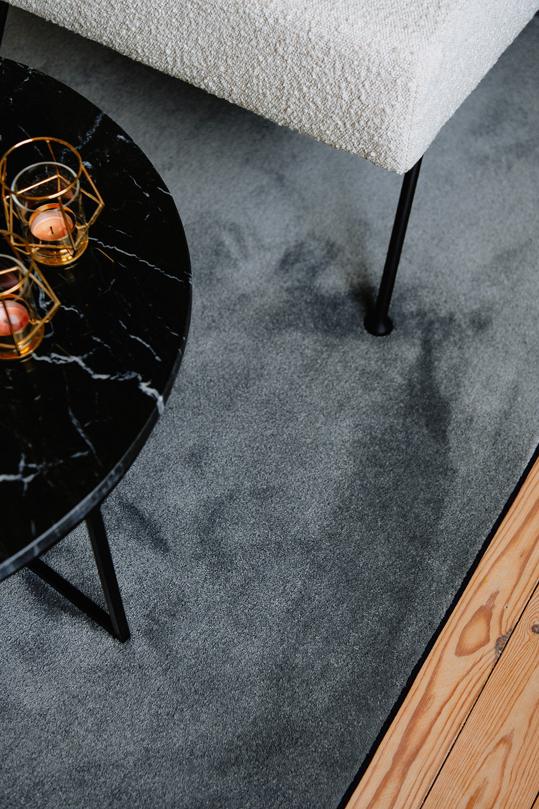 Detail interieur marmeren salontafel op een grijskleurig ecologisch tapijt, op een houten vloer.