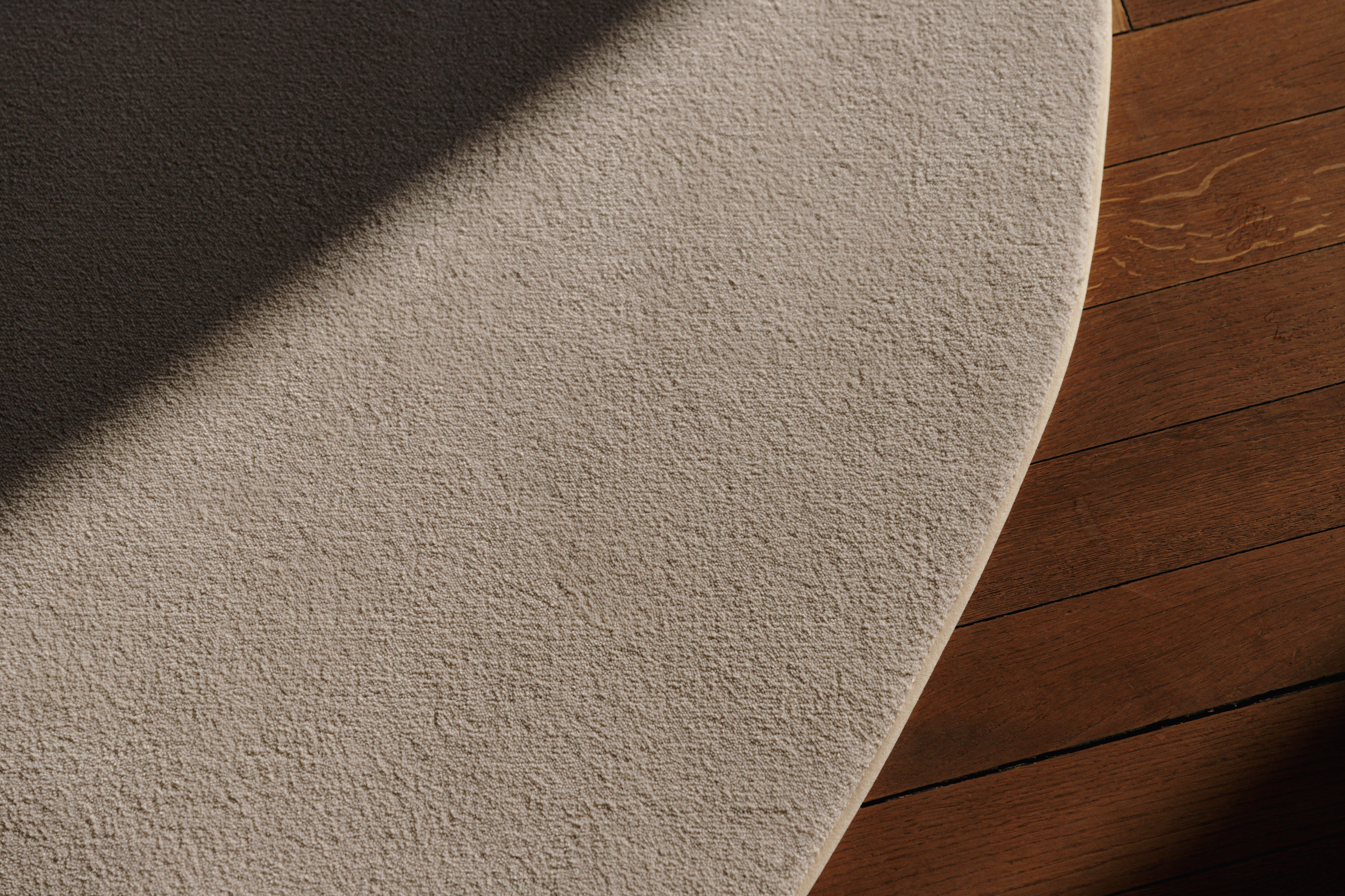 Detail zacht en gerecyceld tapijt met gepersonaliseerde kleurrand met natuurlijk zonlicht op houten vloer.
