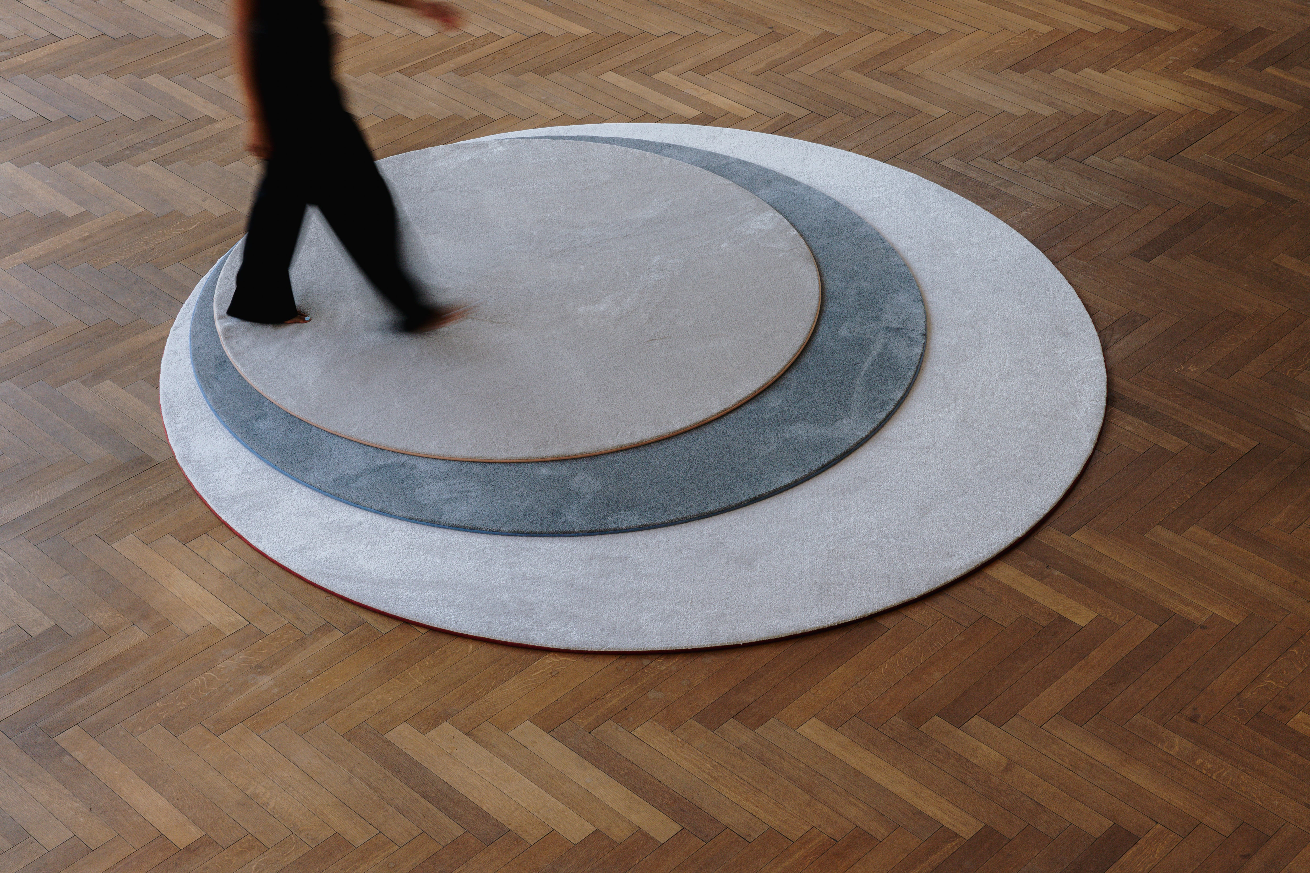Persoon stappend over drie cirkelvormige zachte tapijten op maat in verschillende kleuren.