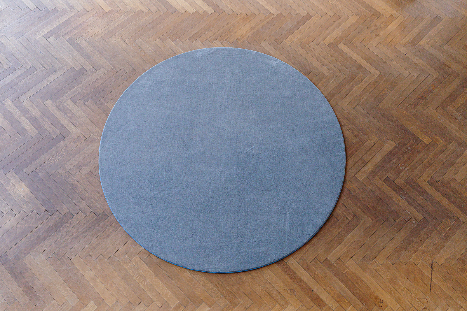 Topshot rond grijs (stone) ecologisch tapijt op parket vloer.