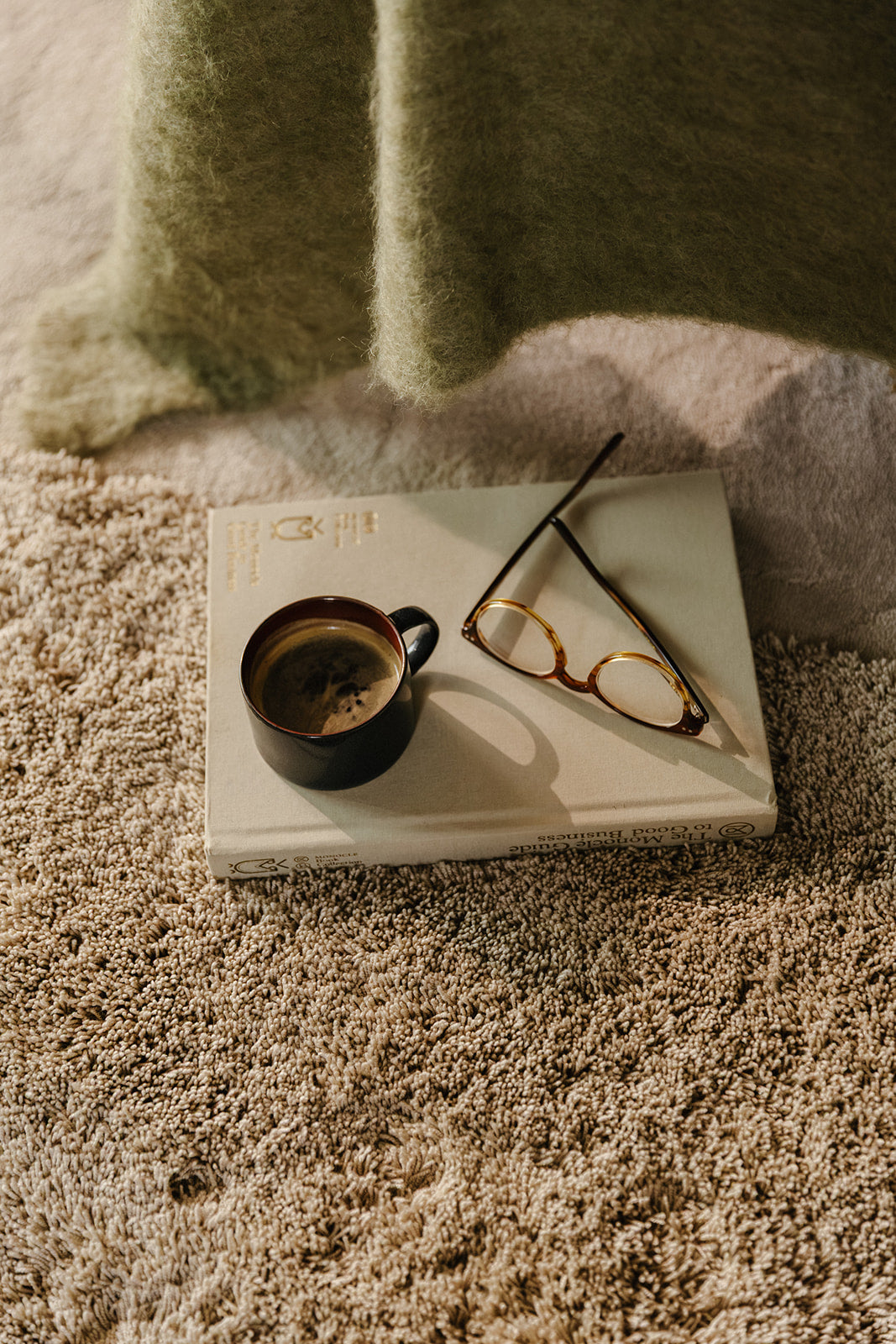 Detail van Rhythm modulair tapijt. Kleuren Dune low Desert high. Boek op tapijt met bril en koffietas.