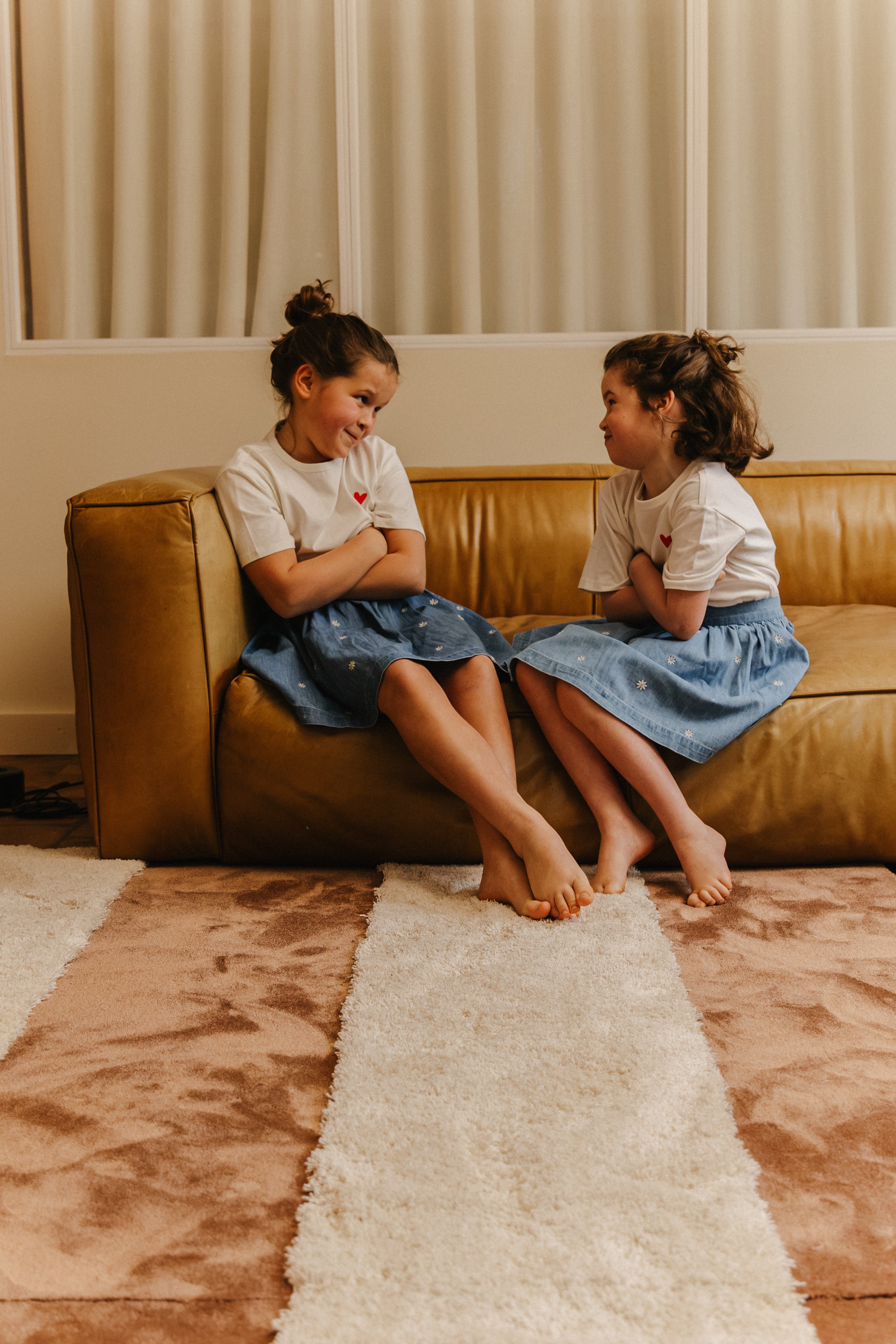 Twee meisjes zitten op een zetel met daarvoor een Rhythm modulair tapijt. Met de kleuren Earth Low en  Moon high.