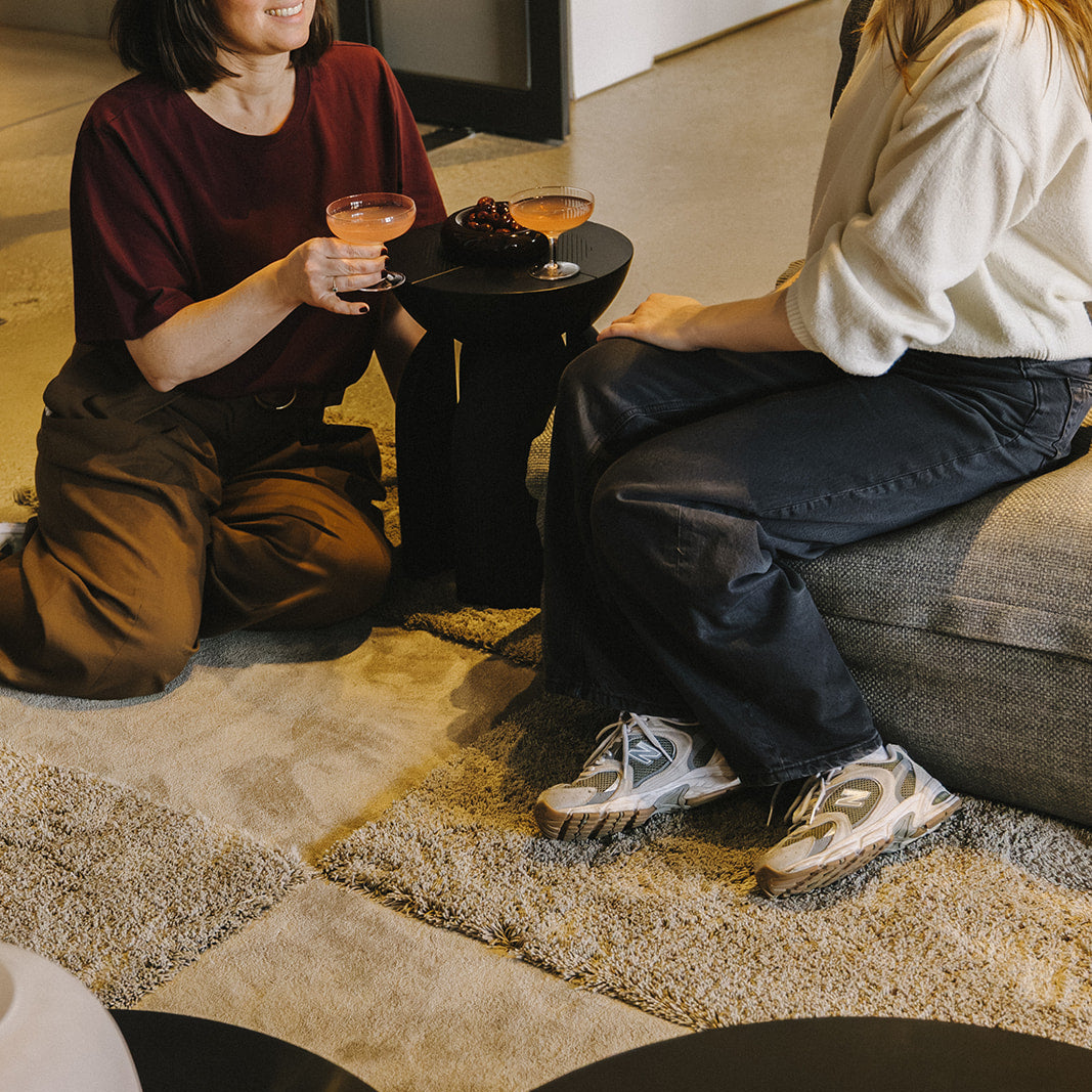 Twee dames die aperetieven op een Rhythm modulair tapijt. Kleuren Clay low & Silt high. Future-proof circulair design.