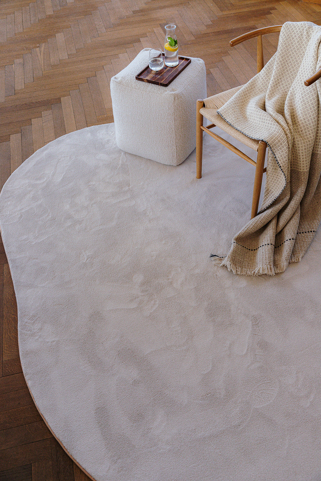 Interieurinspiratie houten vloer met bijzettafel en stoel op organische vorm duurzaam witkleurig tapijt.