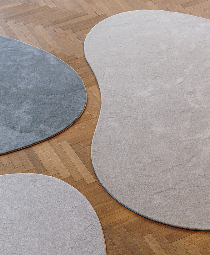 Verschillende maten organische vormen duurzame tapijten op parket vloer in witte (tender), beige (beach) en grijze (stone) kleur.