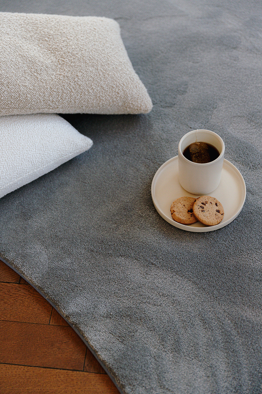 Detail zacht opverend garen grijskleurig stone tapijt, met kussens en een koffiekop.