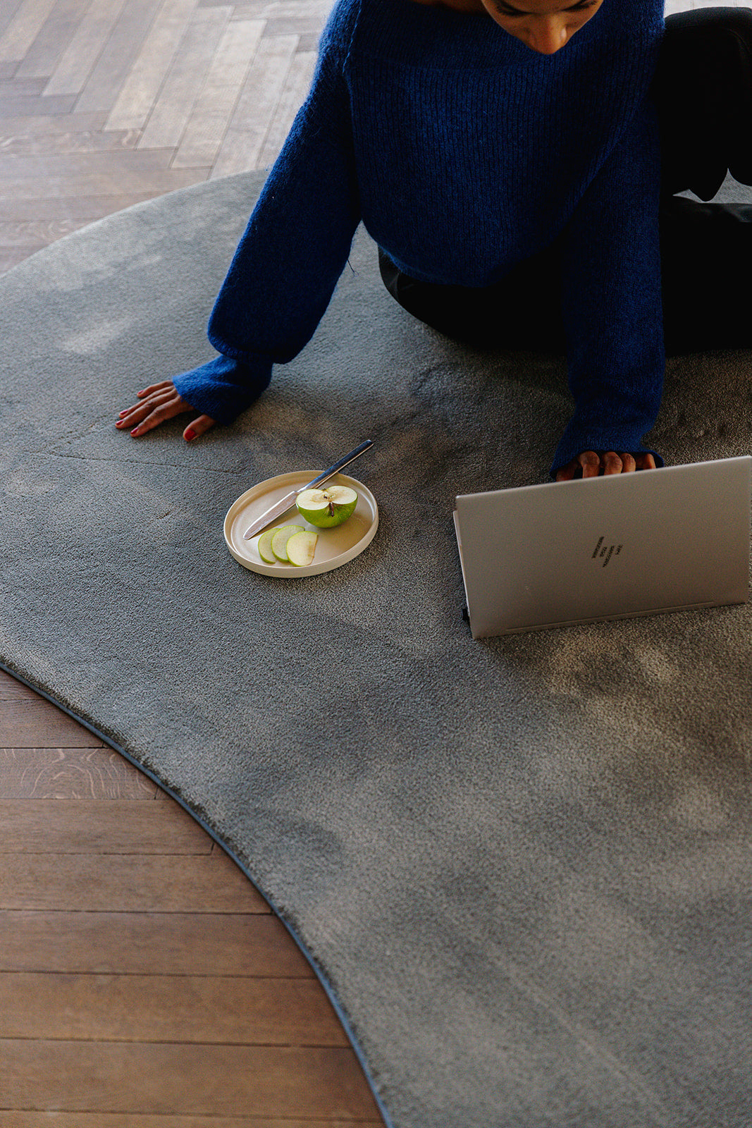 Vrouw zitten op organische vorm circulair tapijt met laptop en fruit.